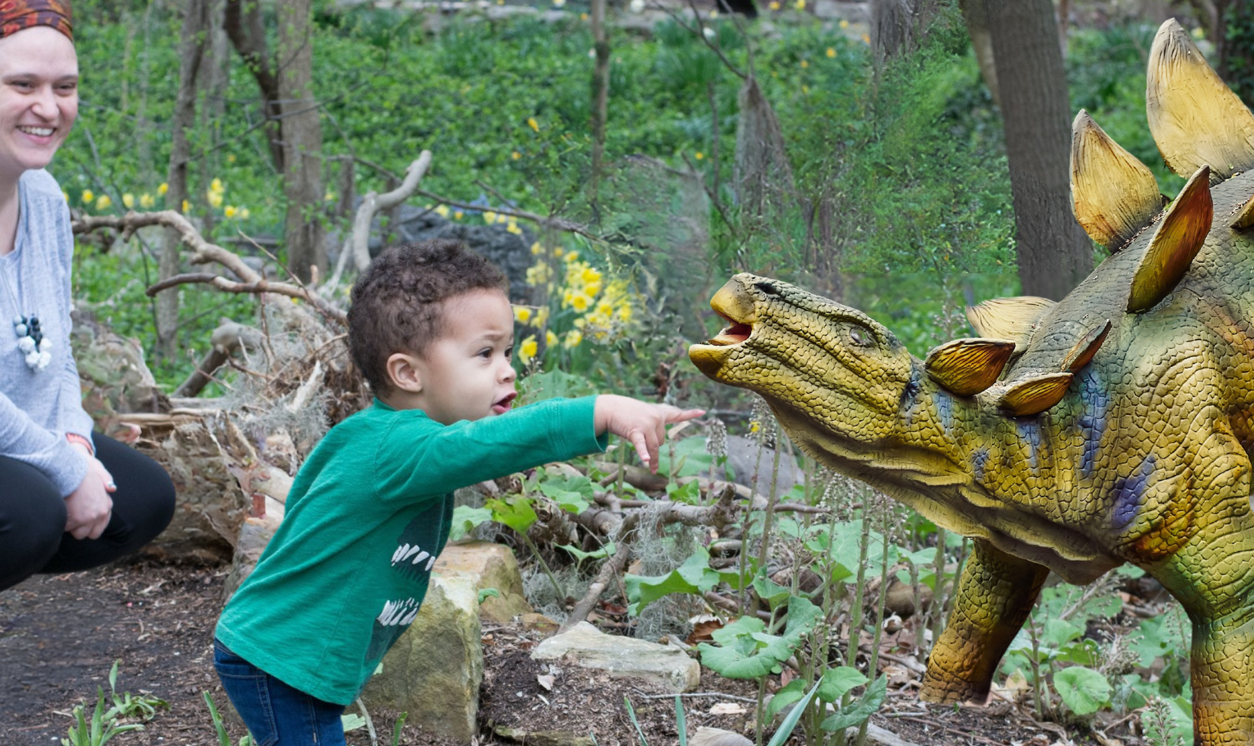 Child looking and pointing at dinosaurs on the Dinosaurs among us trail with parent watching and smiling.