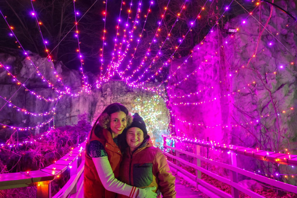 mom and son smiling surrounded by holiday light displays